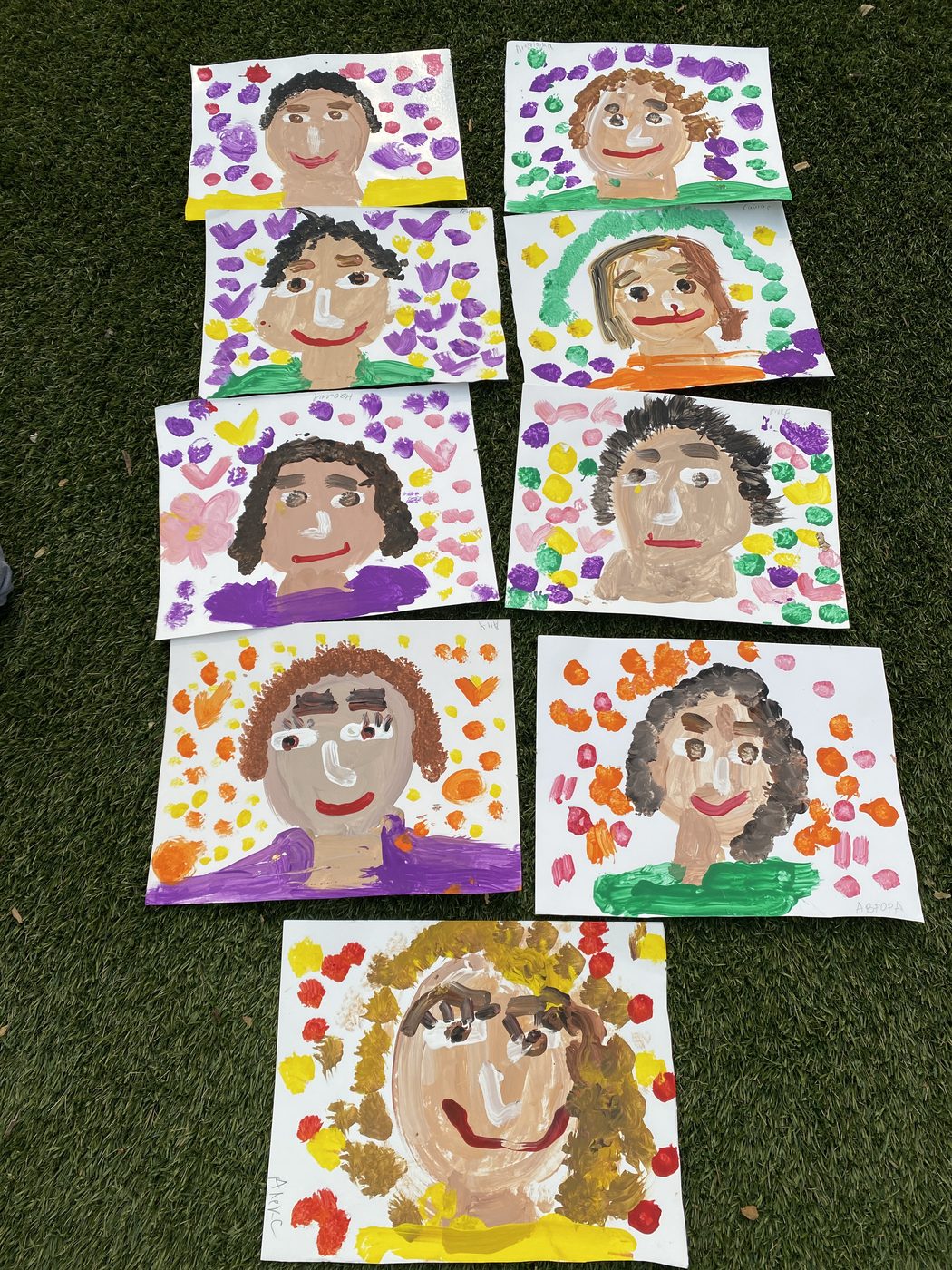 Children's self-portrait paintings displayed on the grass